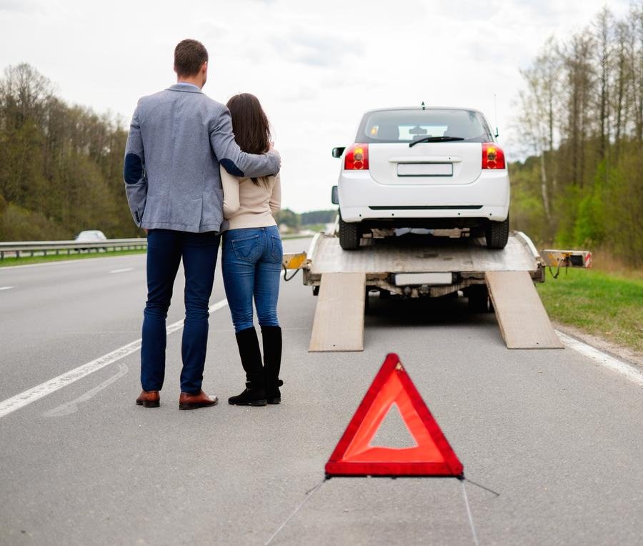 Couple on the side of the road looking at their car on a tow truck